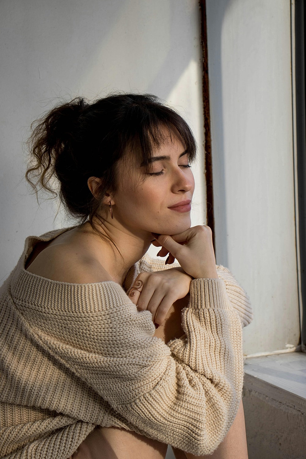 Woman in knitted sweater, thoughtful pose by window.
